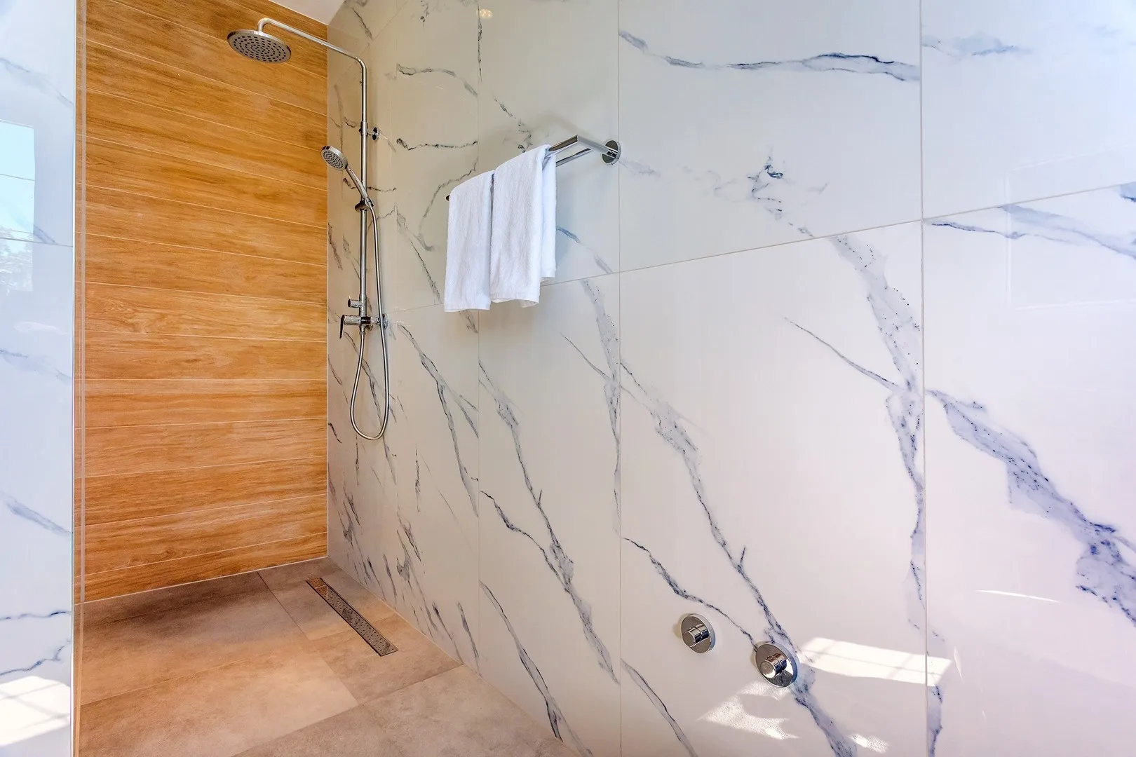 A modern bathroom shower with marble-patterned walls and a wooden accent wall.