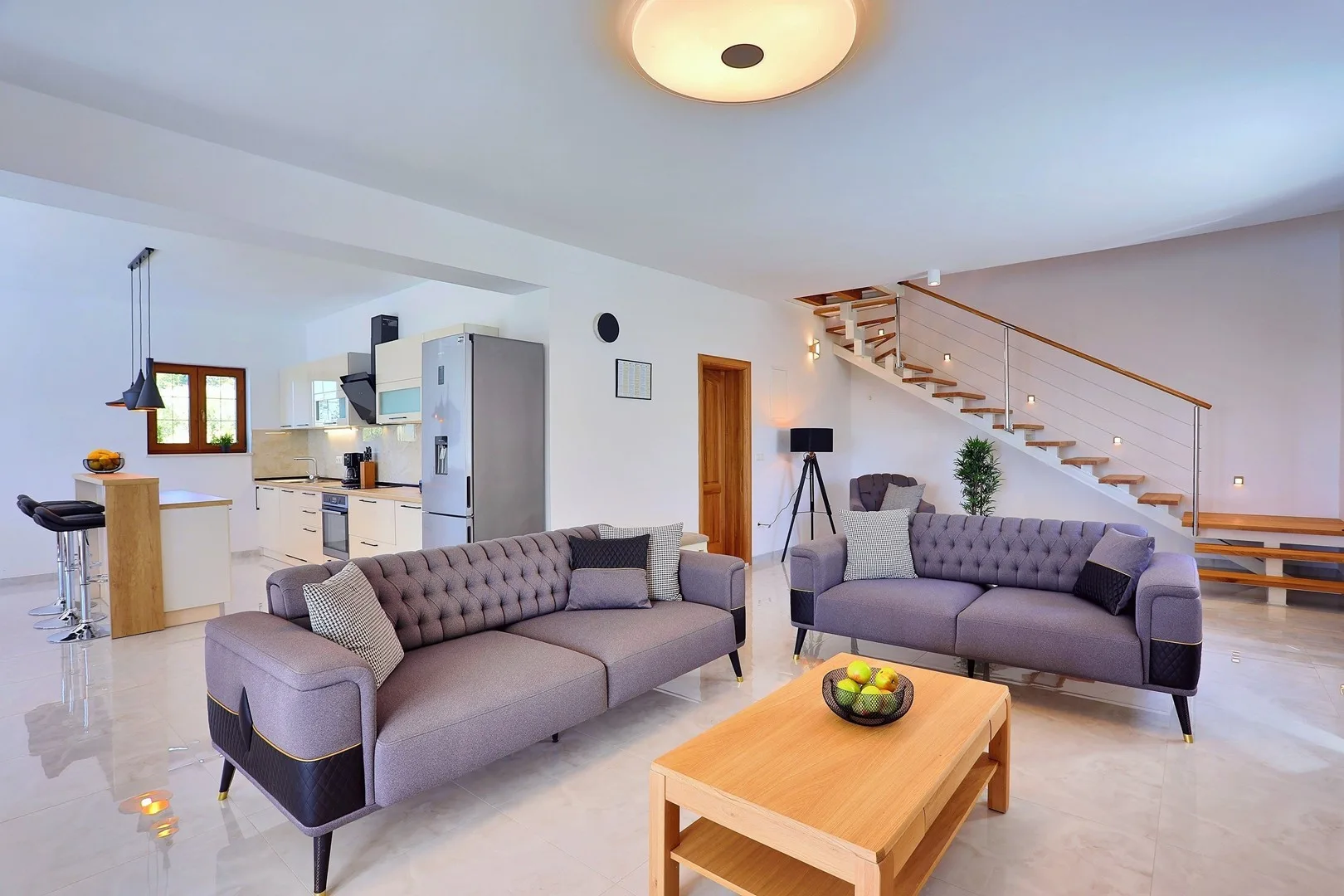 A bright living room with gray seating and an open kitchen.