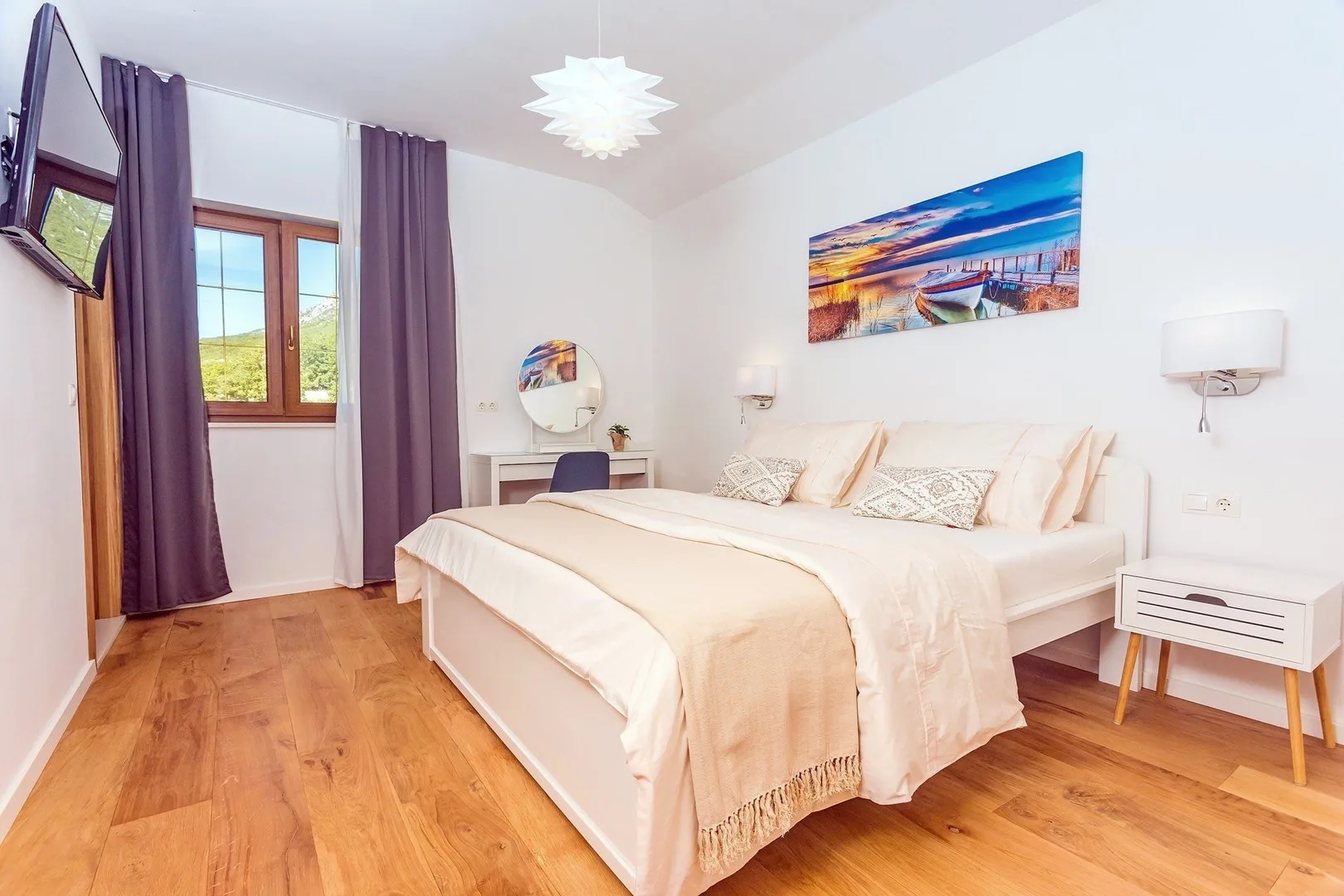 A bright bedroom with a large bed, purple curtains, and wood flooring.