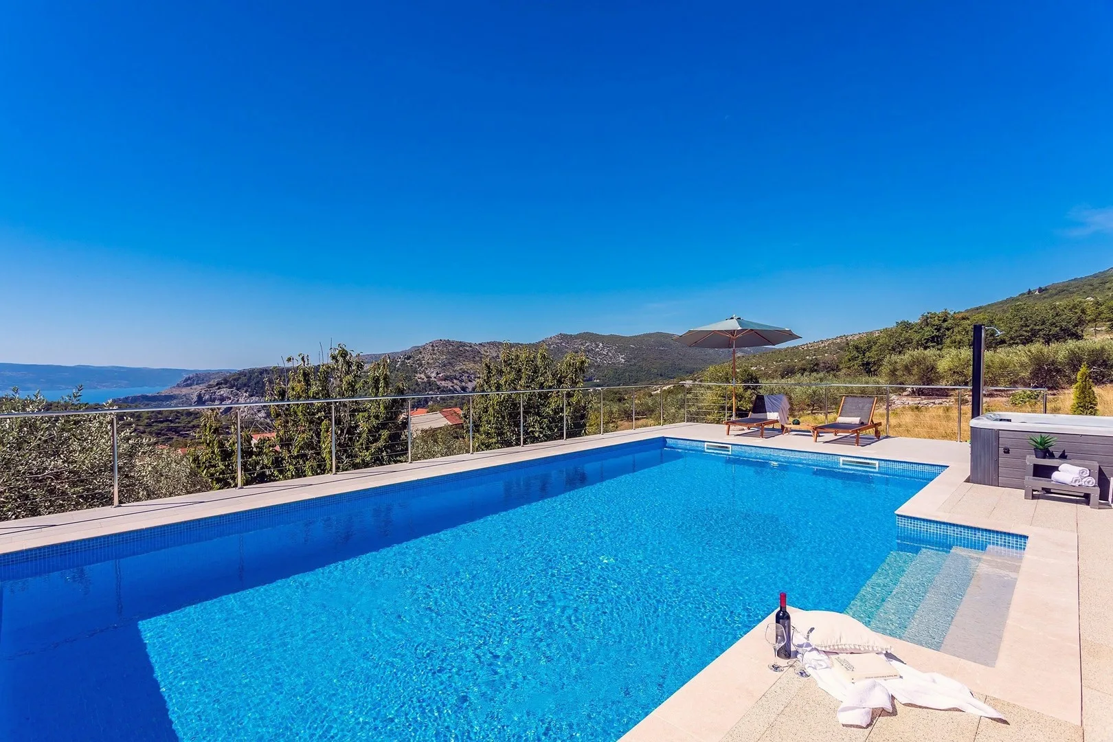 An outdoor swimming pool overlooks a hilly landscape beneath a clear blue sky.
