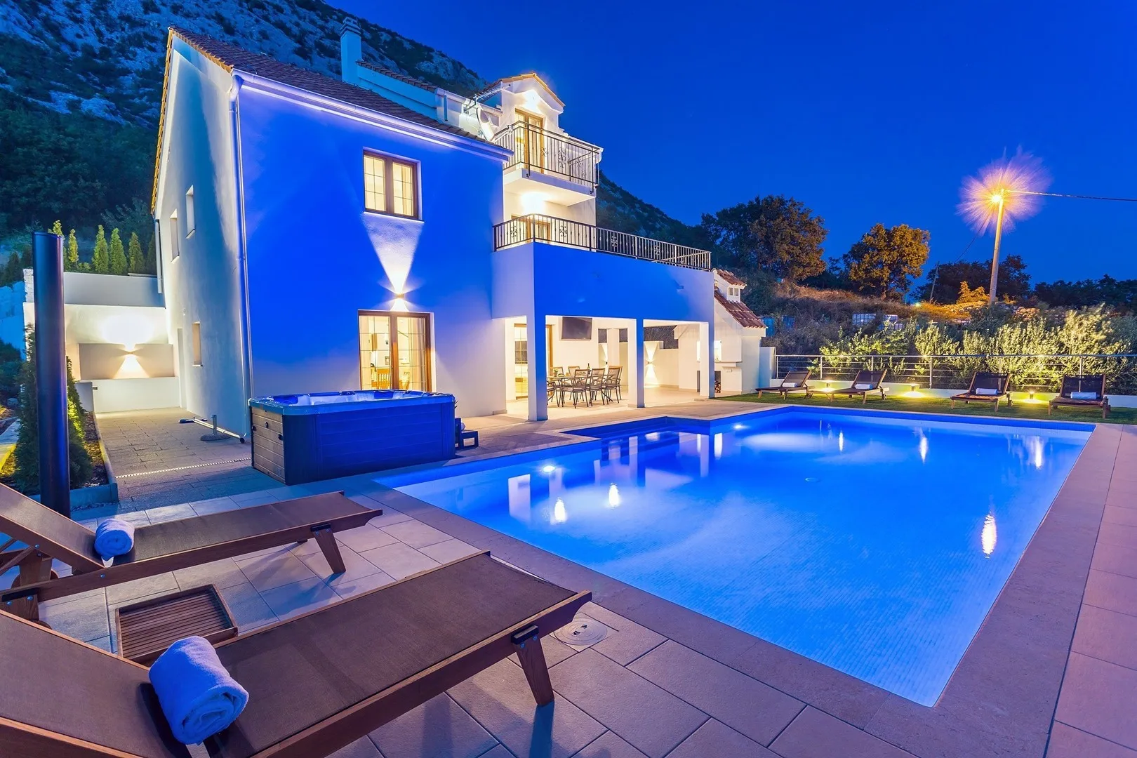 A modern house overlooks an illuminated swimming pool at night.