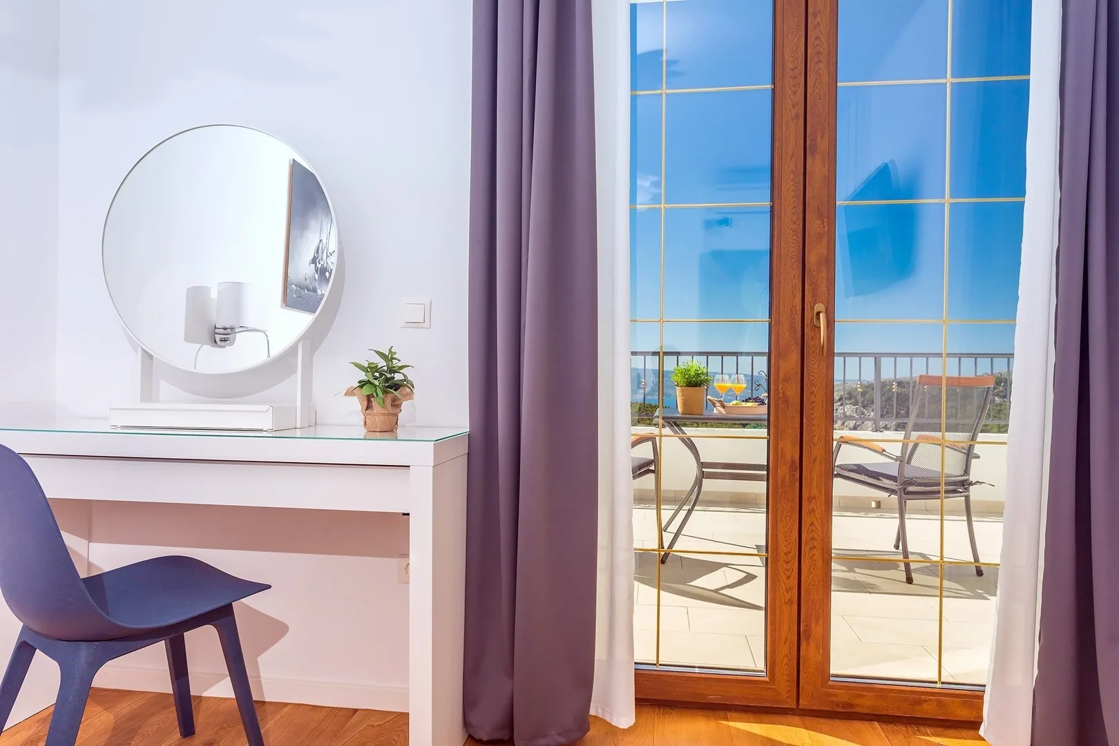 A bright room has a desk and chair beside glass doors opening onto a balcony.