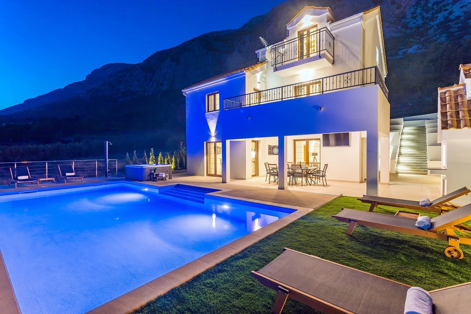 A modern house stands beside an illuminated swimming pool at dusk.