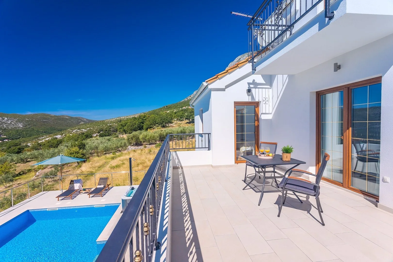 A sunny terrace overlooks a swimming pool and green hills.