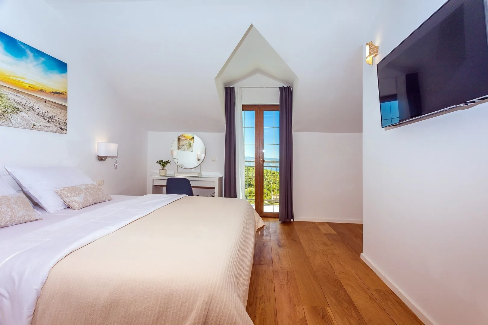 A bright bedroom with a bed, a dressing table, and glass doors opening to a balcony.