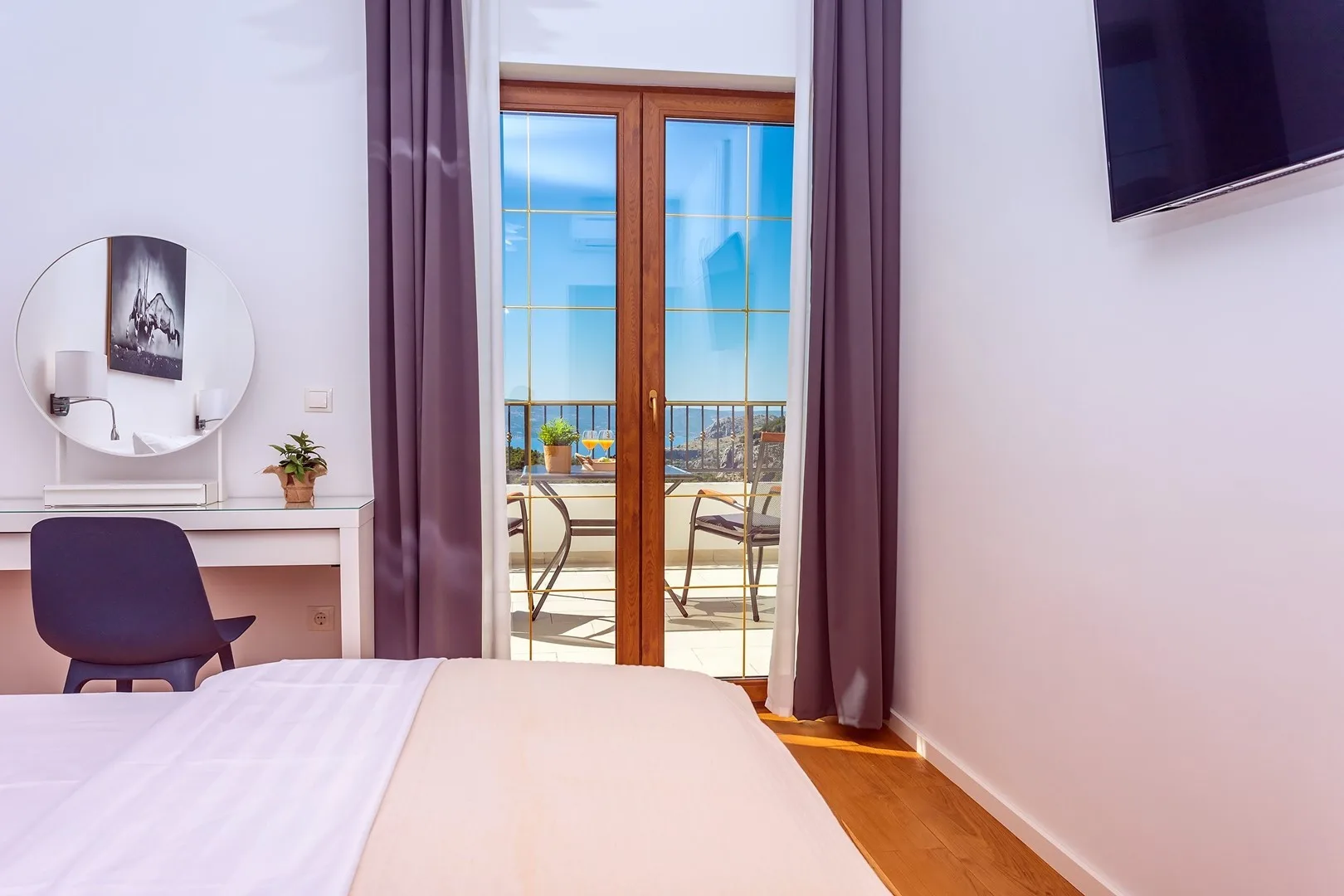 A bedroom with a bed, desk, and glass doors opening onto a balcony.