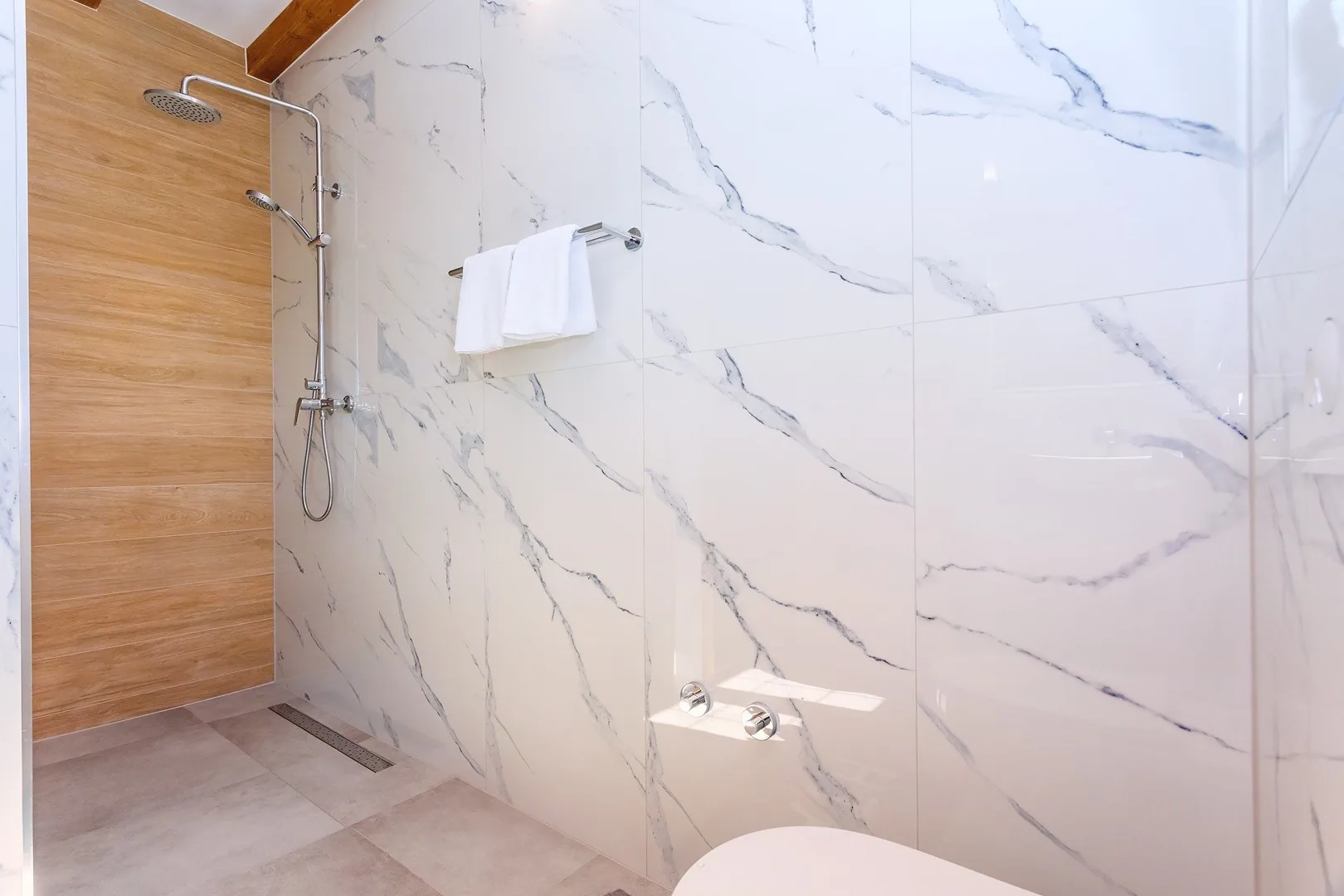 A tiled bathroom shower with a handheld fixture and towel on the wall.