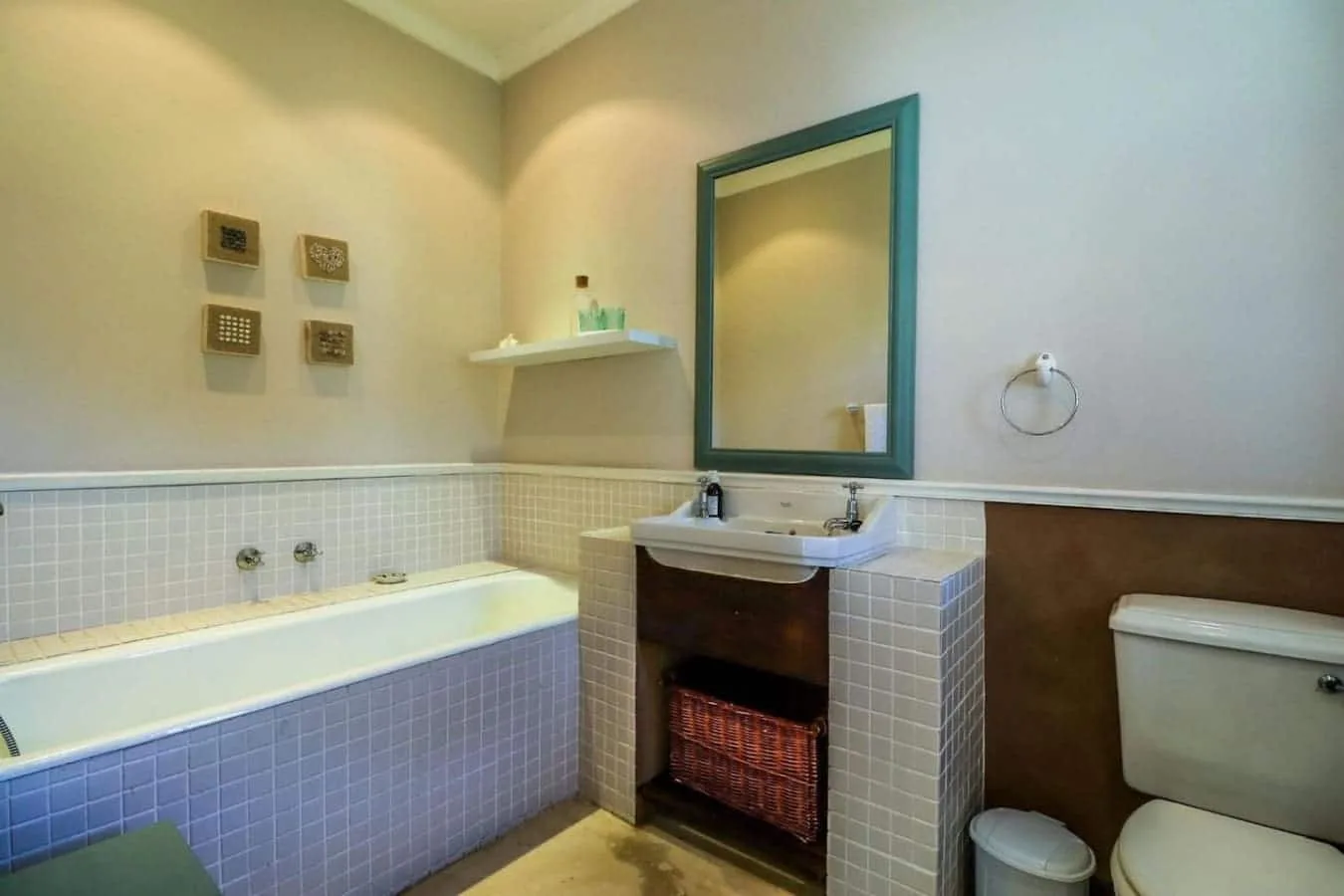 A tiled bathroom with a bathtub, a sink beneath a framed mirror, and a toilet.