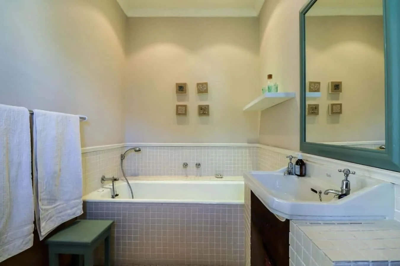 A tiled bathroom features a bathtub, a sink beneath a large mirror, and towels hanging nearby.