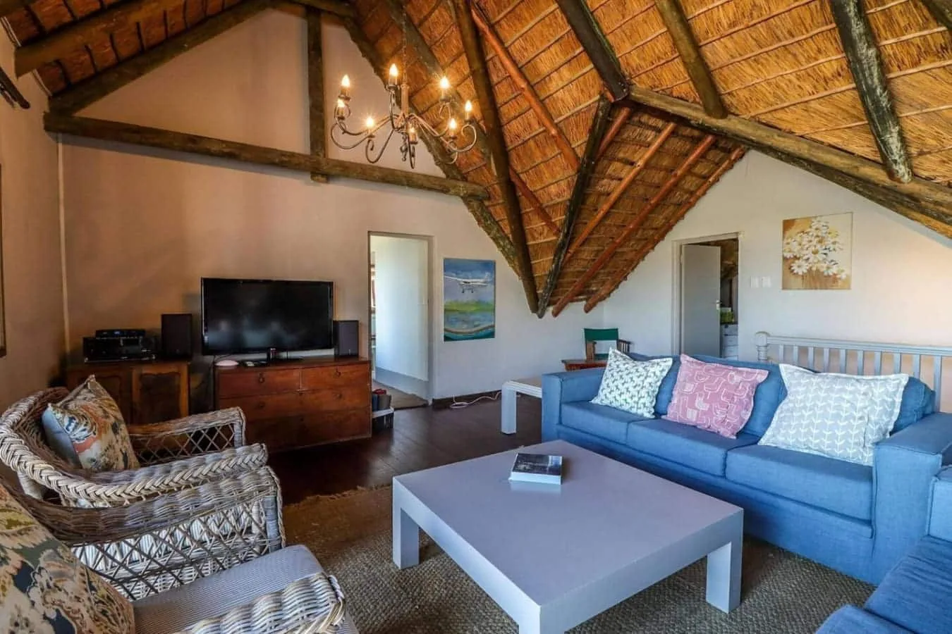 A living room with a blue sofa, wicker chairs, a television, and a high thatched ceiling.
