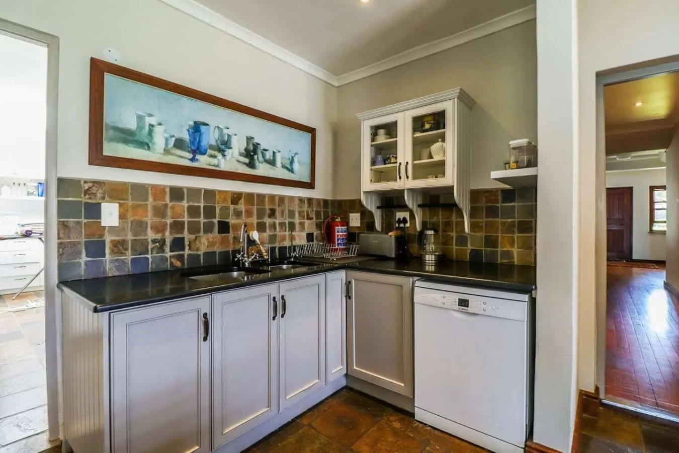 A compact kitchen with white cabinets, dark countertops, a tiled backsplash, and a dishwasher.