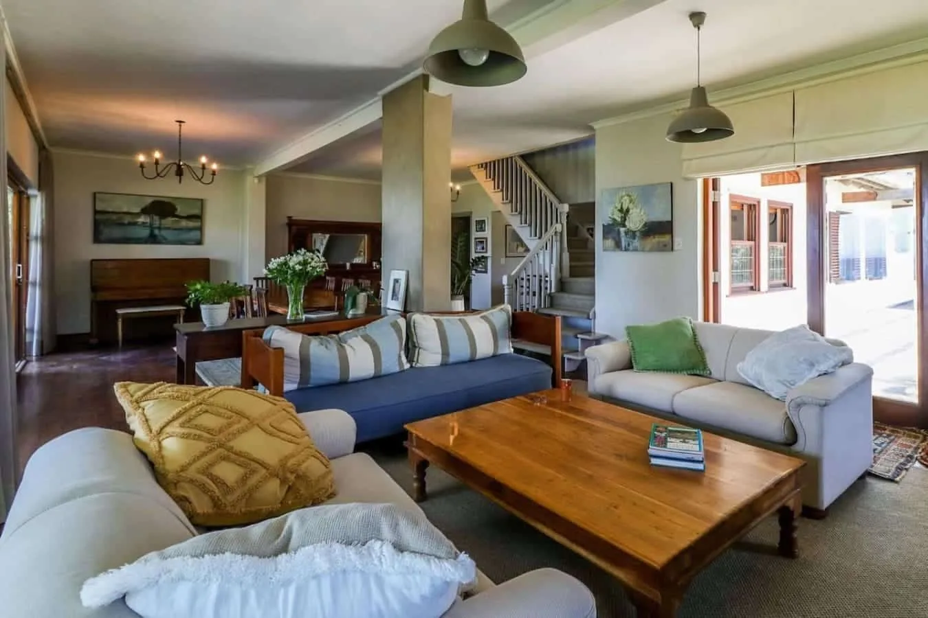 A bright open-plan living room has sofas around a wooden coffee table, with a staircase and dining area beyond.