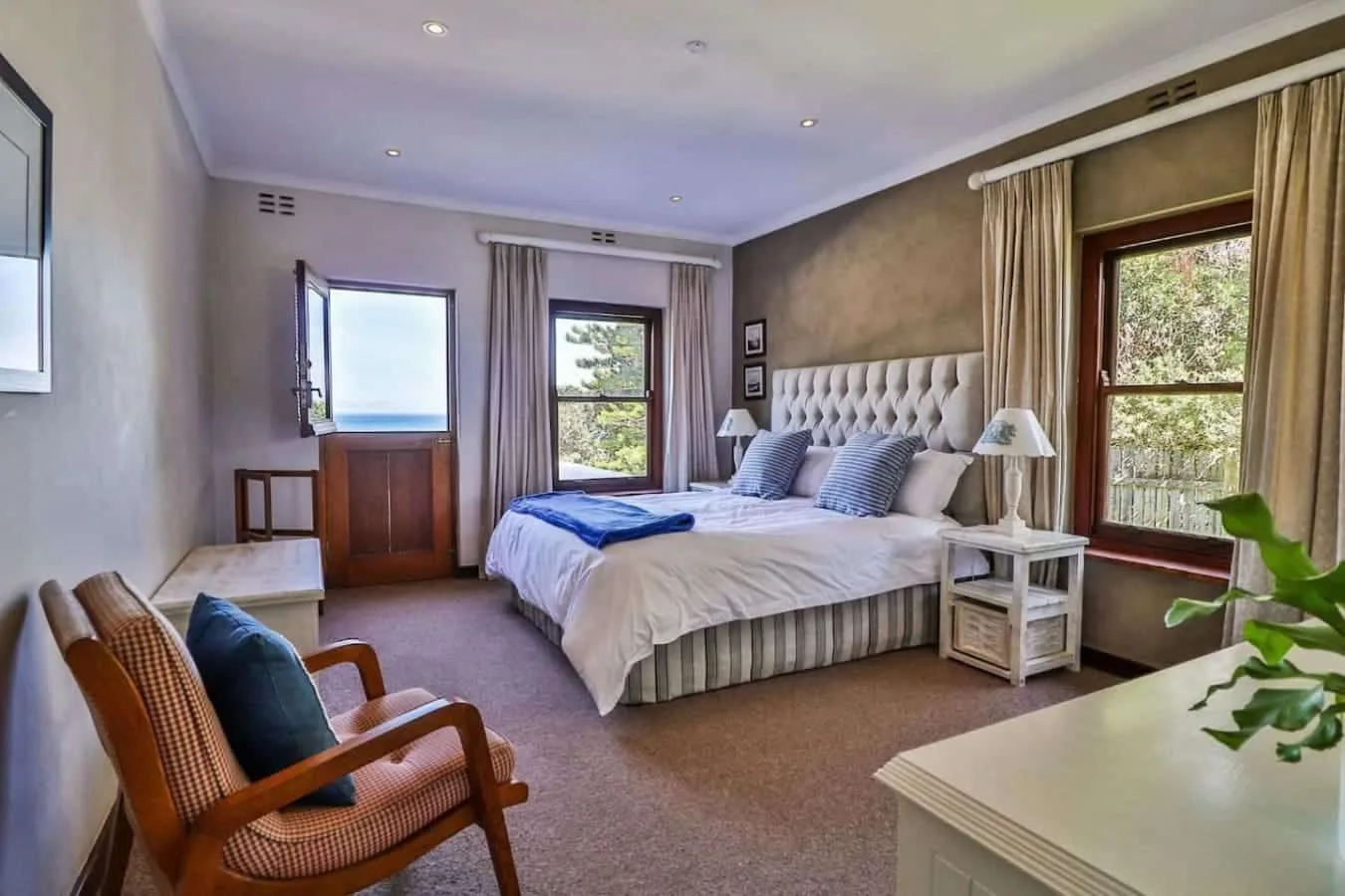A bedroom with a large bed, bedside tables, curtained windows, and a woven armchair.
