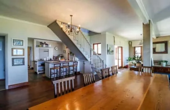 A dining table fills the foreground of an open kitchen and dining area beneath a staircase.