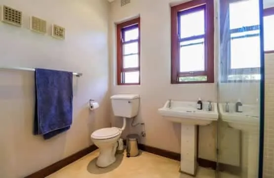 A bathroom with a toilet, pedestal sink, three tall windows, and a towel hanging on the wall.