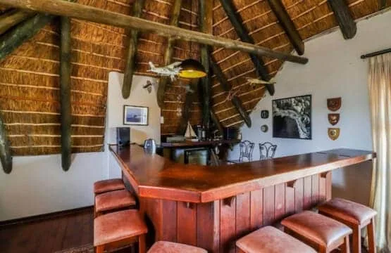 A wooden bar with stools sits beneath a steep thatched ceiling and exposed beams.