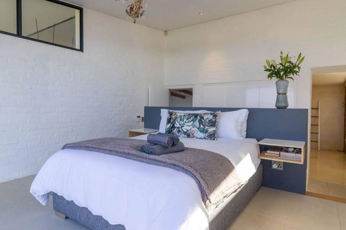 A bright bedroom with a neatly made bed and leafy plant on the headboard.
