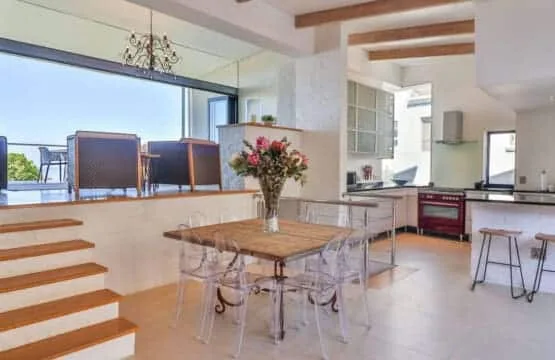 A bright open-plan kitchen and dining area with a wooden table and large windows.