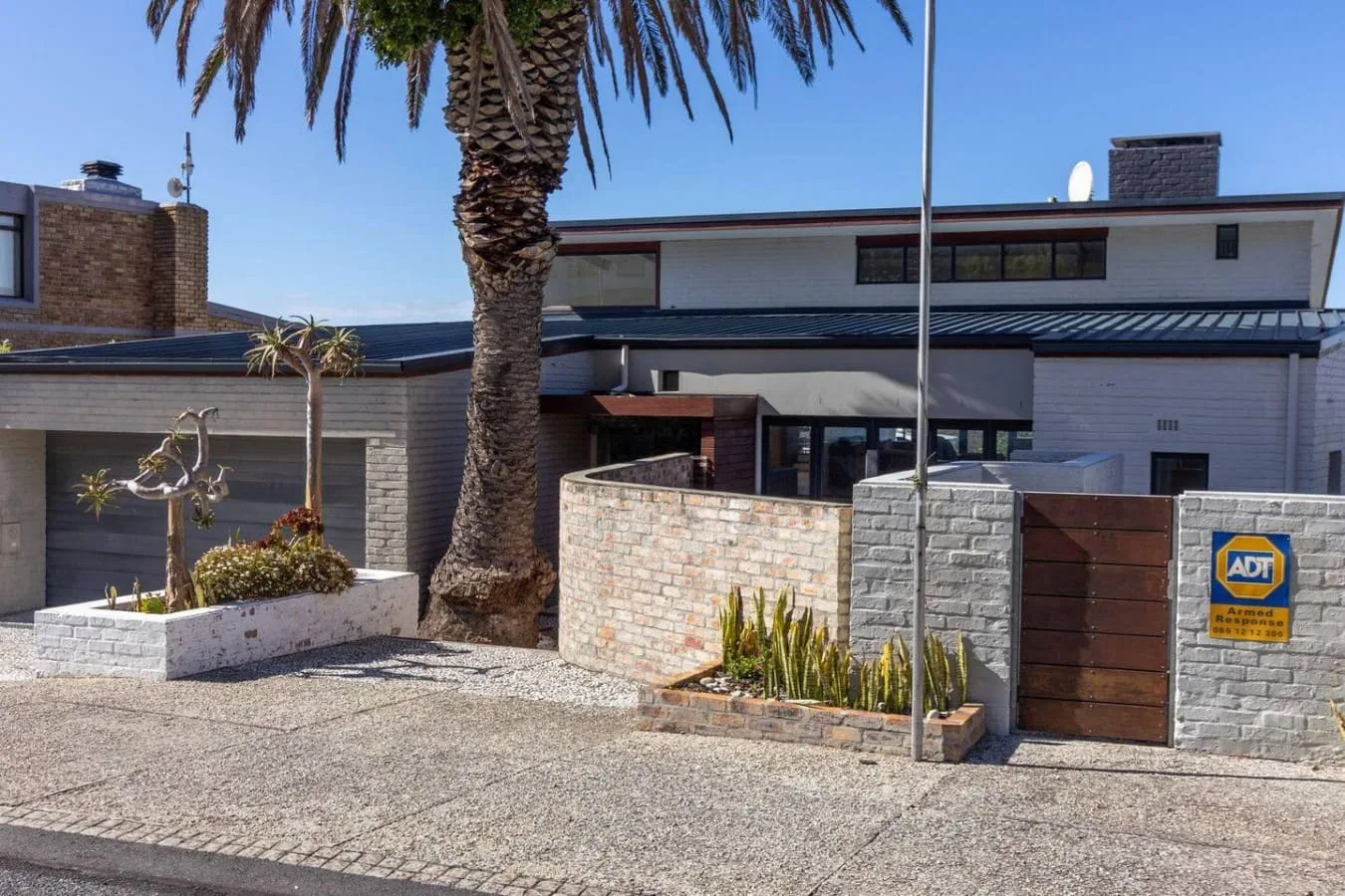 A modern house exterior with a paved driveway and a palm tree.