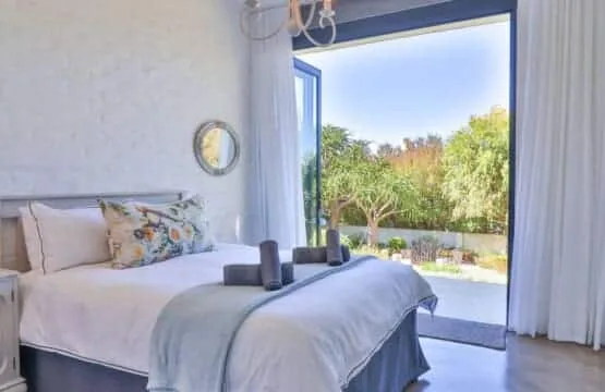 A bedroom with a neatly made bed beside open doors overlooking a garden.