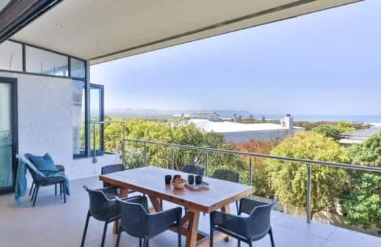 An outdoor dining area overlooks green treetops and distant hills.