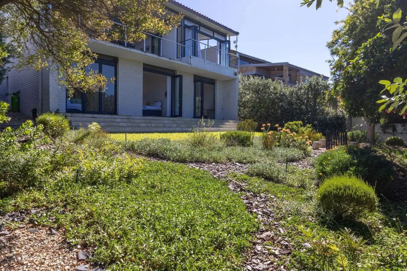 A modern house stands behind a landscaped garden with shrubs and greenery.