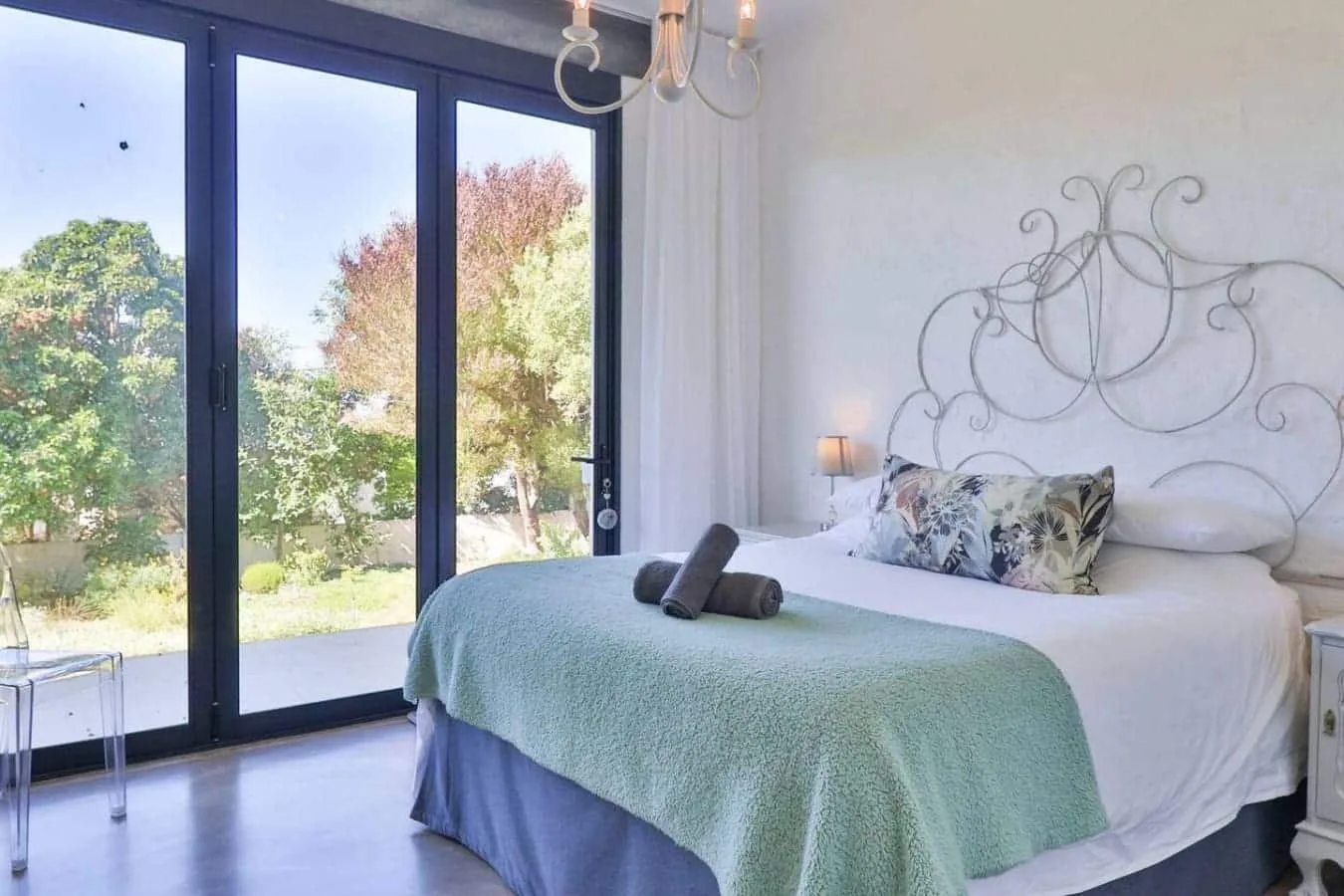 A bedroom with a bed beside large glass doors overlooking a garden.