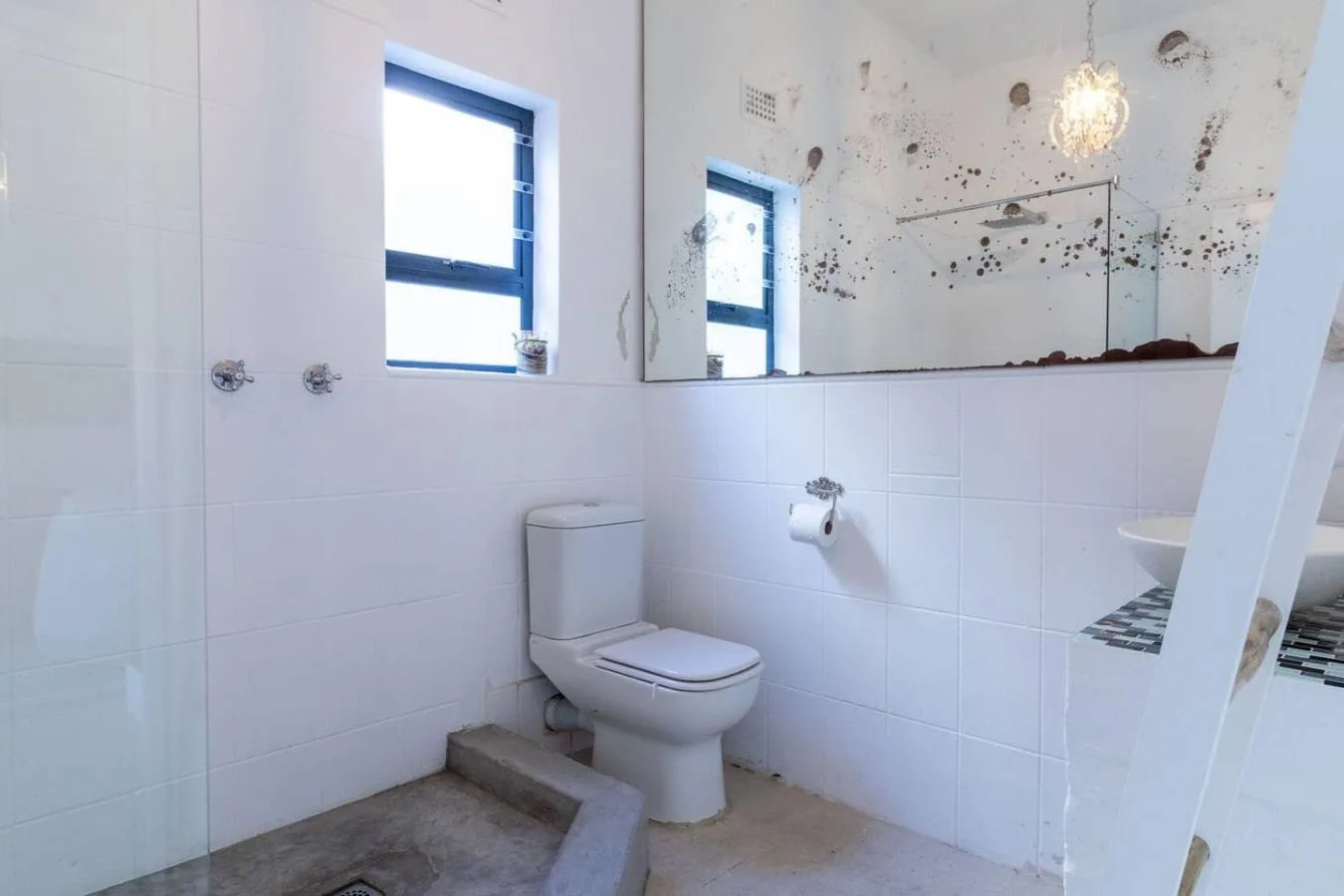 A tiled bathroom with a toilet, wall mirror, and window.