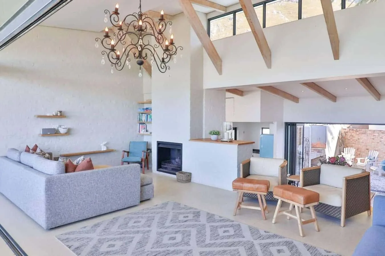 A bright living room with high timber beams and a seating area around a fireplace.