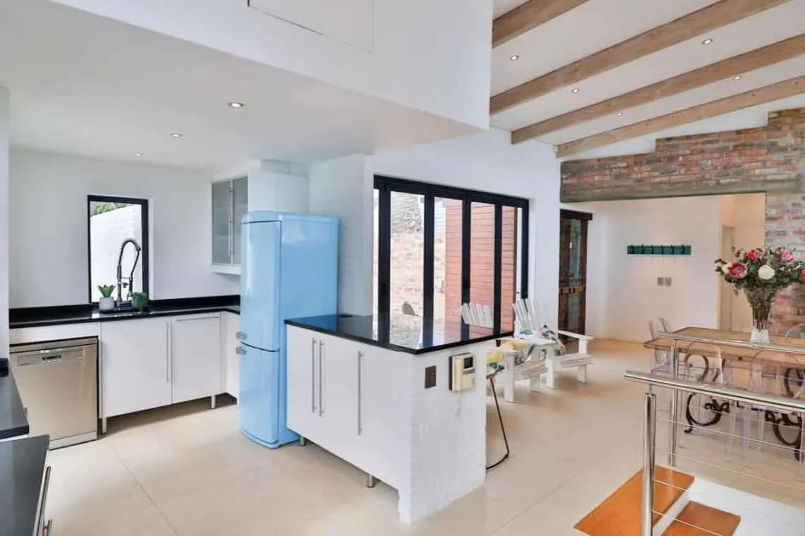A bright kitchen with white cabinets and a central island opens onto a dining area.