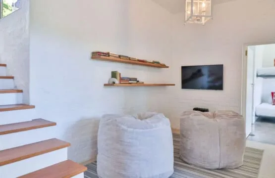 A bright living area with cushioned seating, wall shelves, and a television.