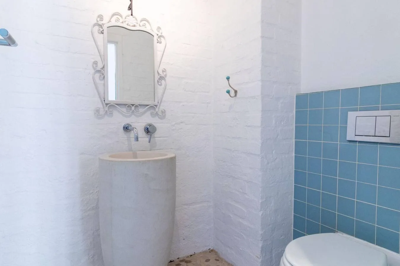 A bathroom with a pedestal sink, ornate mirror, and blue tiled wall.