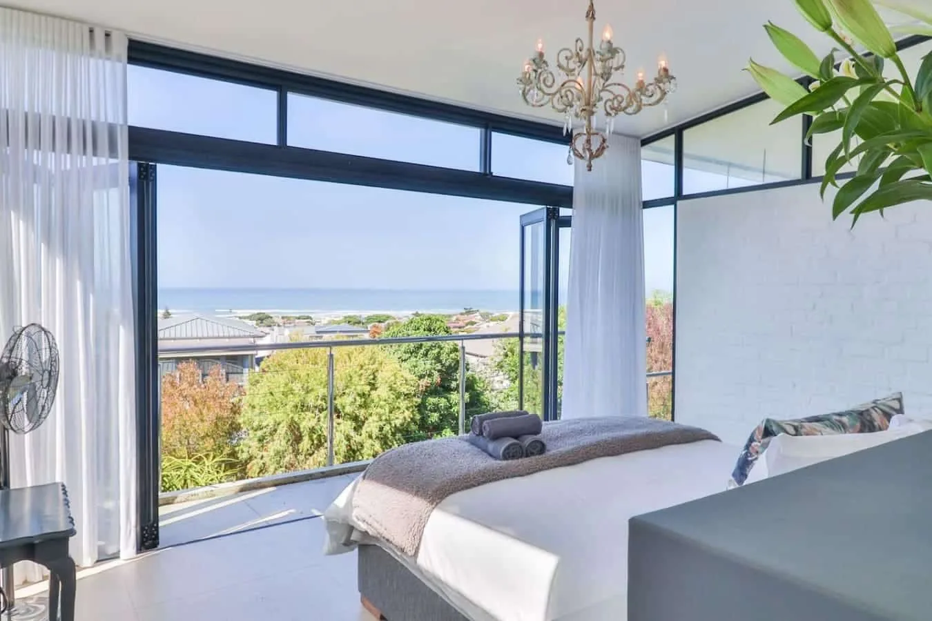 A bright bedroom opens onto a balcony with leafy views and the sea beyond.