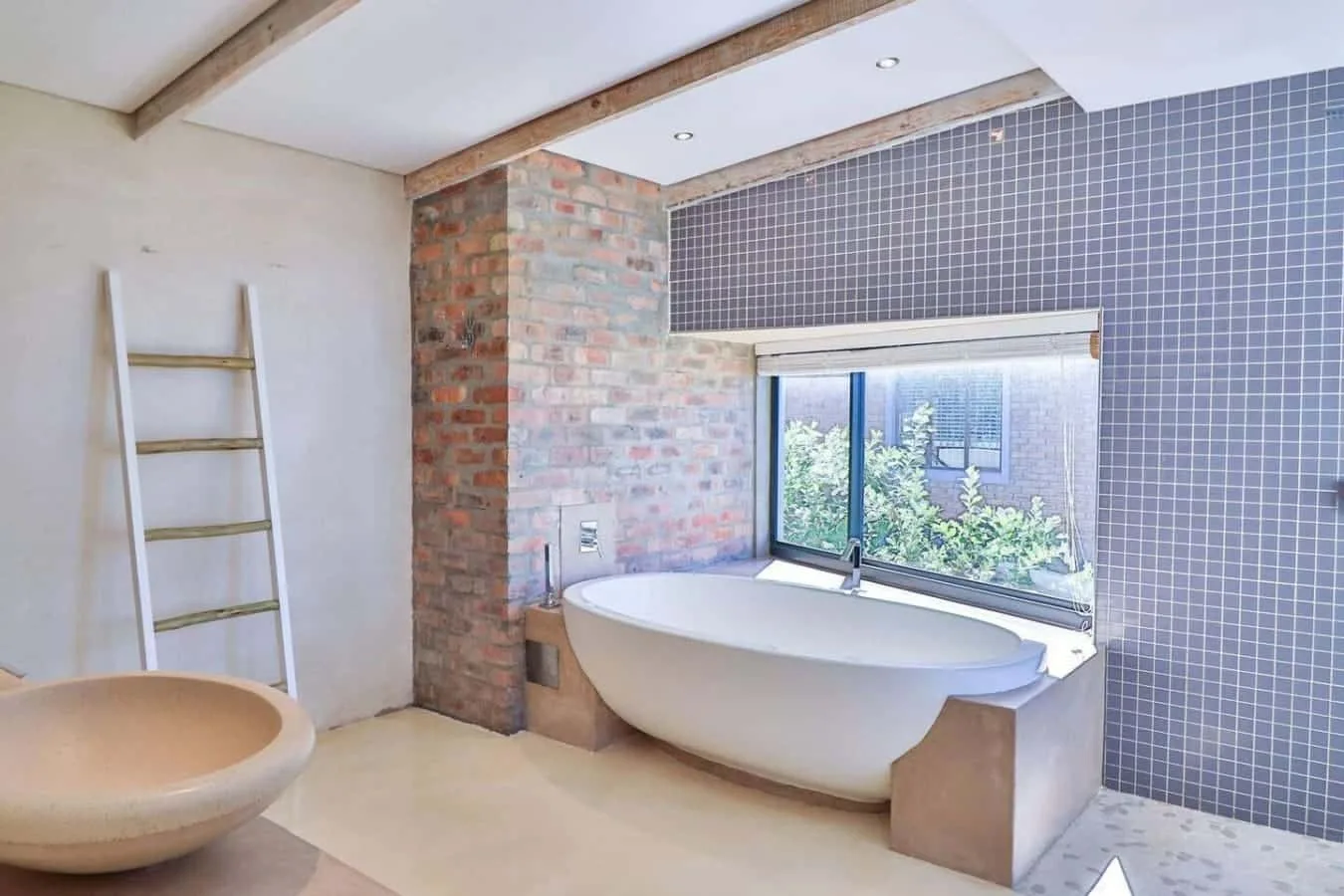 A bathroom features a freestanding bathtub beneath a wide window.