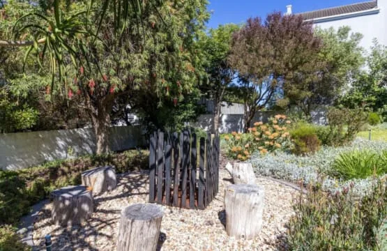 A landscaped garden features gravel paths, trees, and rustic seating.