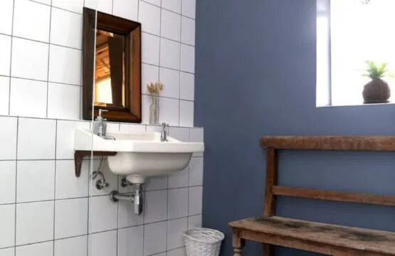 Un baño alicatado con un lavabo de pared y un banco de madera.