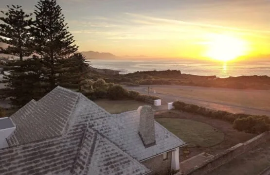 El techo de una casa costera y unos árboles miran al océano al atardecer.