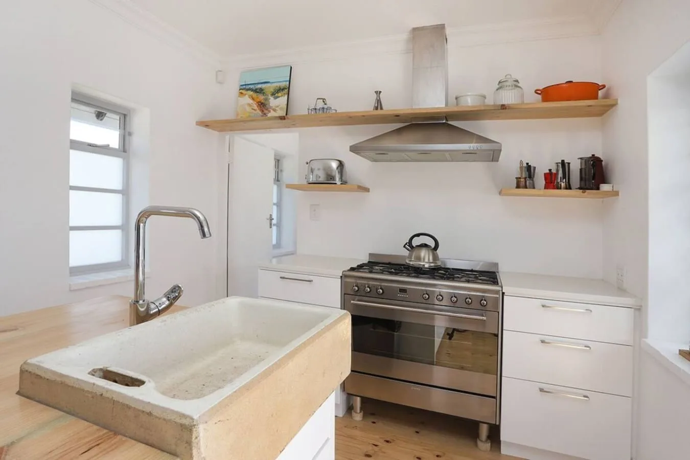 Una cocina luminosa con un fregadero grande, una estufa y estantes en la pared.