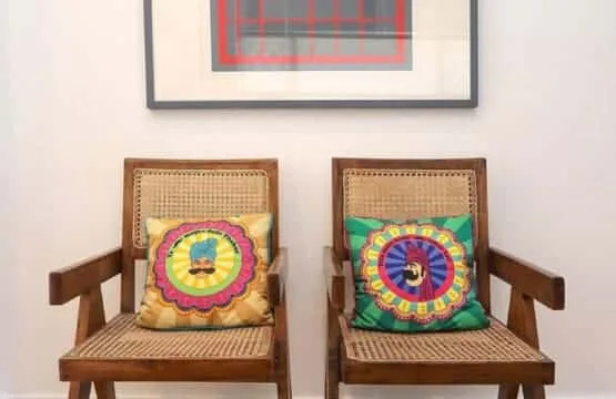 Dos sillas de madera con cojines coloridos están bajo un cuadro enmarcado.