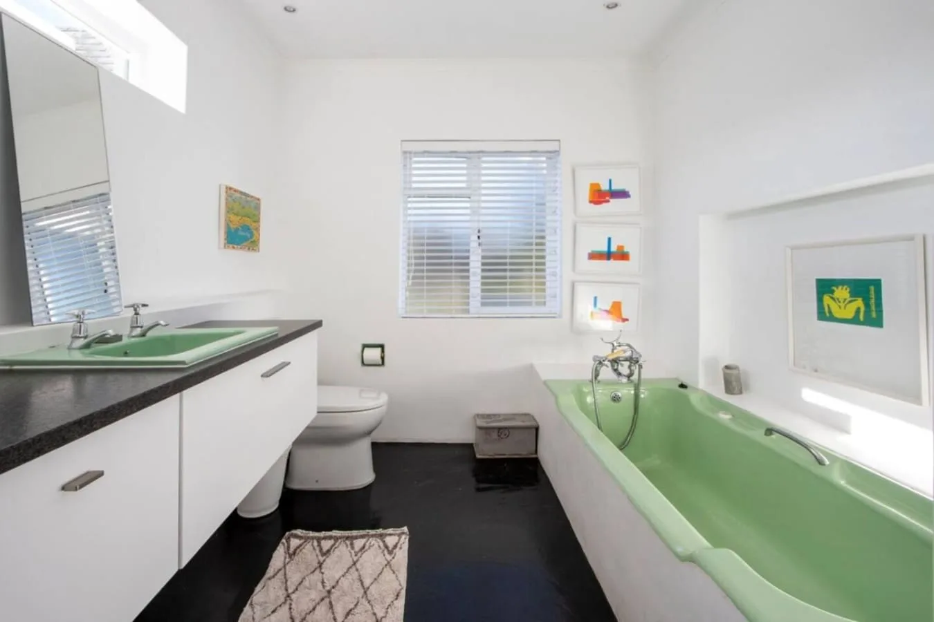 Un baño luminoso con bañera verde, lavabo y persianas en la ventana.