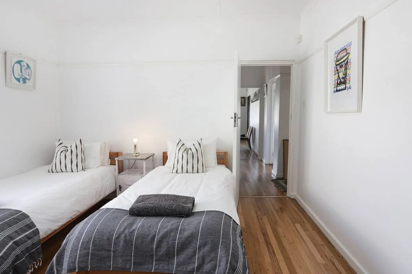 Un dormitorio luminoso con dos camas y un pasillo visible a través de la puerta.