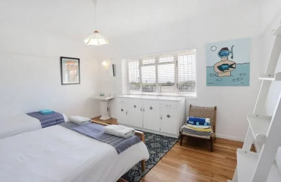 Un dormitorio luminoso con una cama, una ventana y una pequeña zona para sentarse.