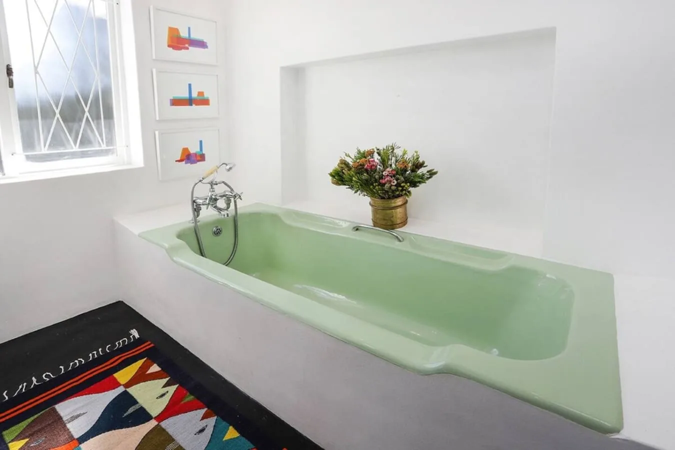 Un baño con una bañera verde pálido y un arreglo de flores.