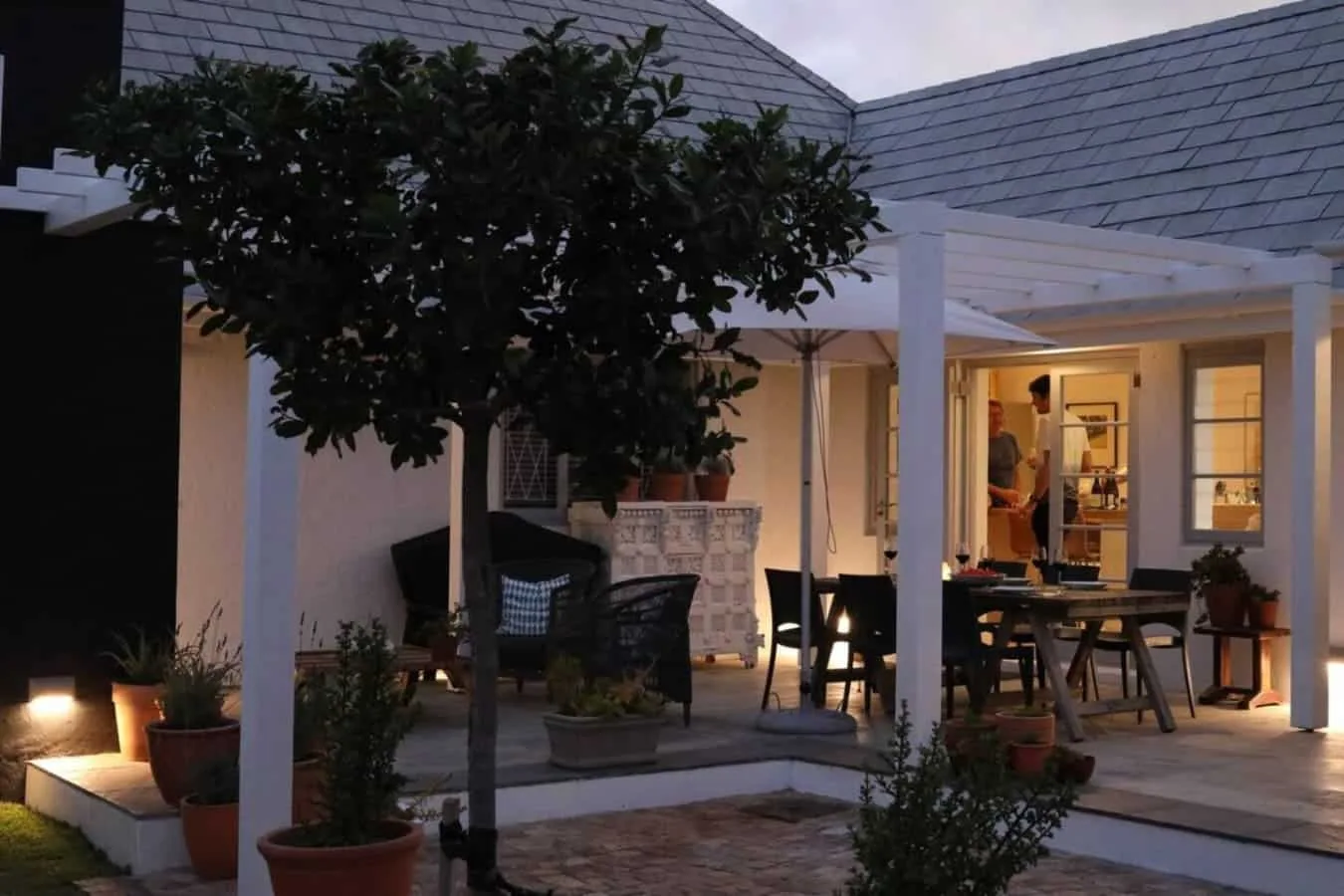 Un patio exterior cubierto con asientos y plantas en macetas junto a un edificio iluminado.