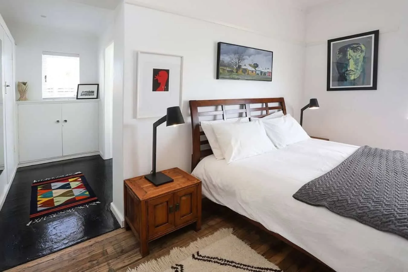 Dormitorio con una cama bien tendida, mesita de madera y cuadros enmarcados.