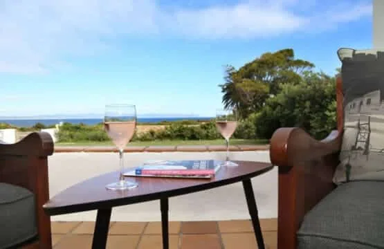 Una mesa de patio con bebidas mira al mar bajo un cielo azul.