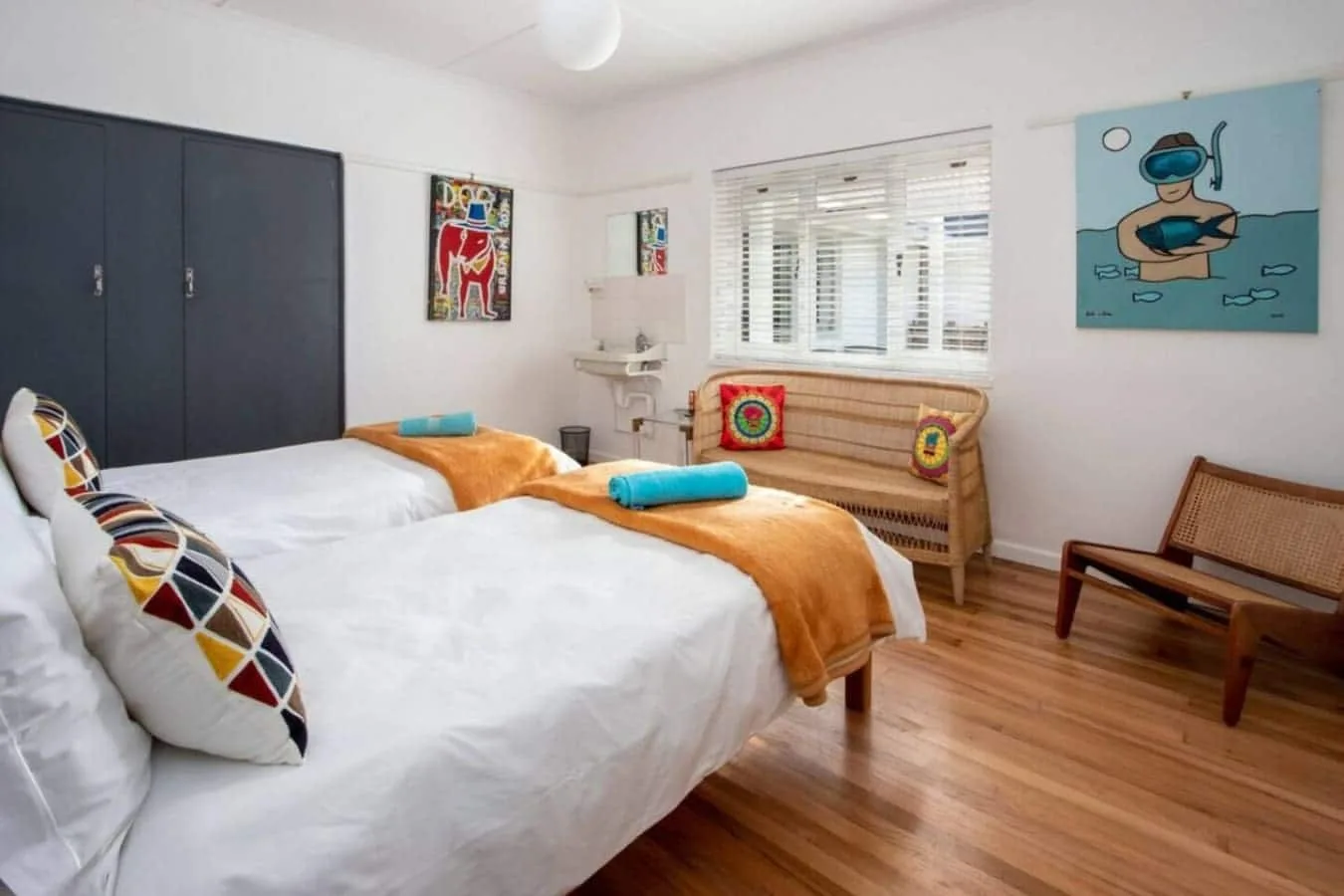 Un dormitorio luminoso tiene dos camas con ropa de cama blanca y mantas naranjas.