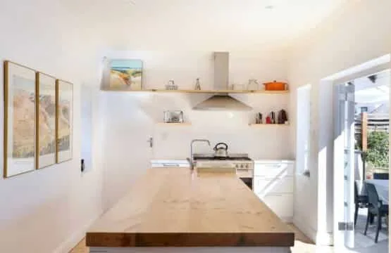 Una cocina luminosa con una isla larga, estantes abiertos y una puerta de vidrio hacia un patio.