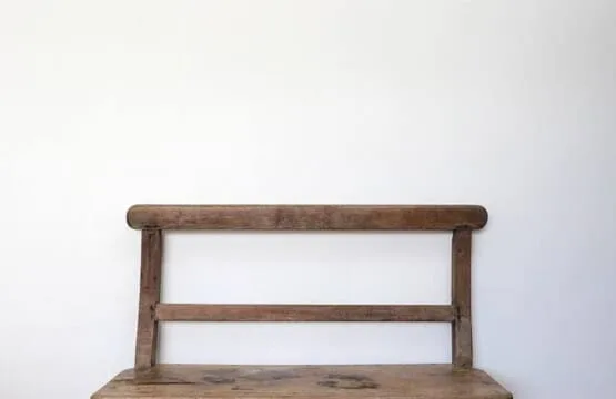 Un banco de madera está junto a una pared lisa de color claro.