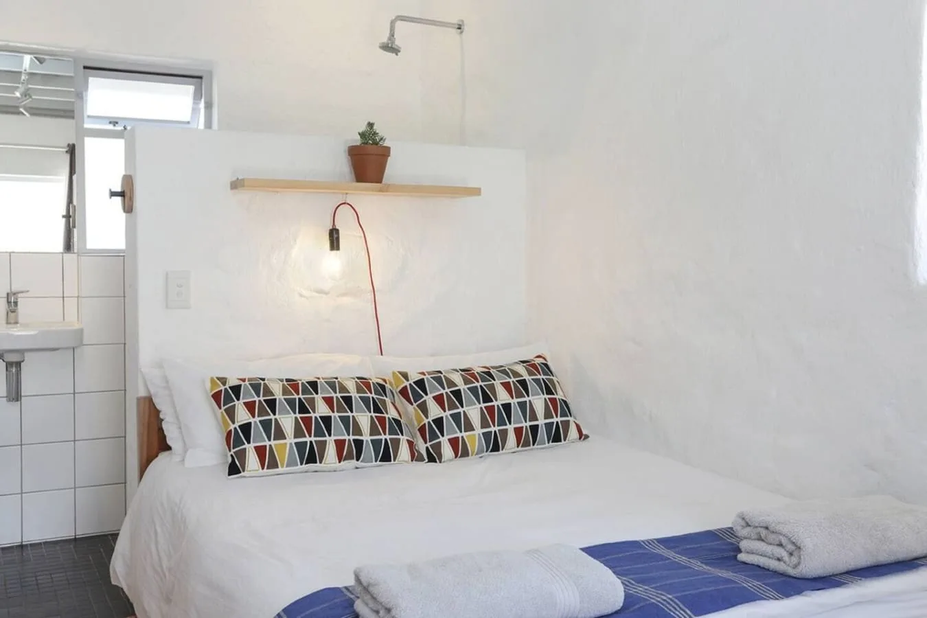 Un dormitorio con una cama, almohadas estampadas y una pequeña repisa sobre el cabecero.